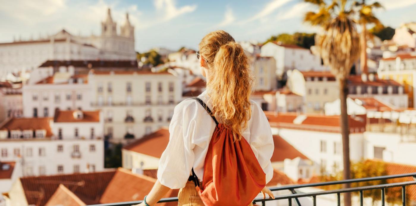 Una ragazza di spalle guarda la città di Lisbona da un punto panoramico durante una giornata di sole