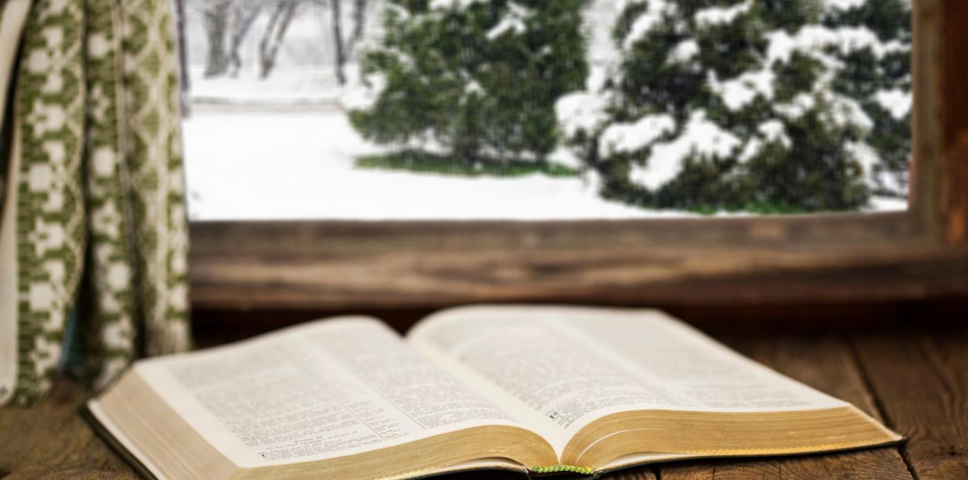 Un libro aperto sul davanzale di una finestra, oltre la quale si vede un paesaggio ricoperto di neve