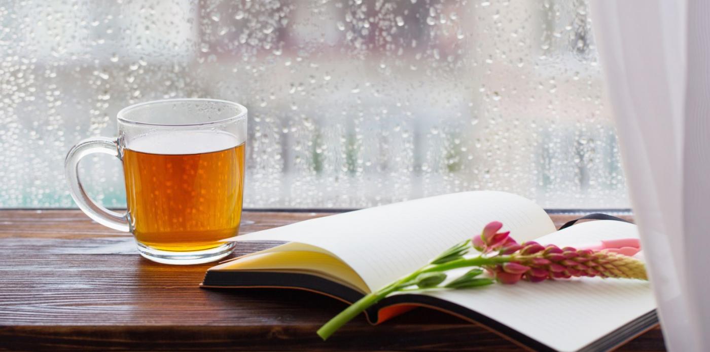 Un libro aperto sul davanzale di una finestra accanto a una tazza di tè mentre fuori piove