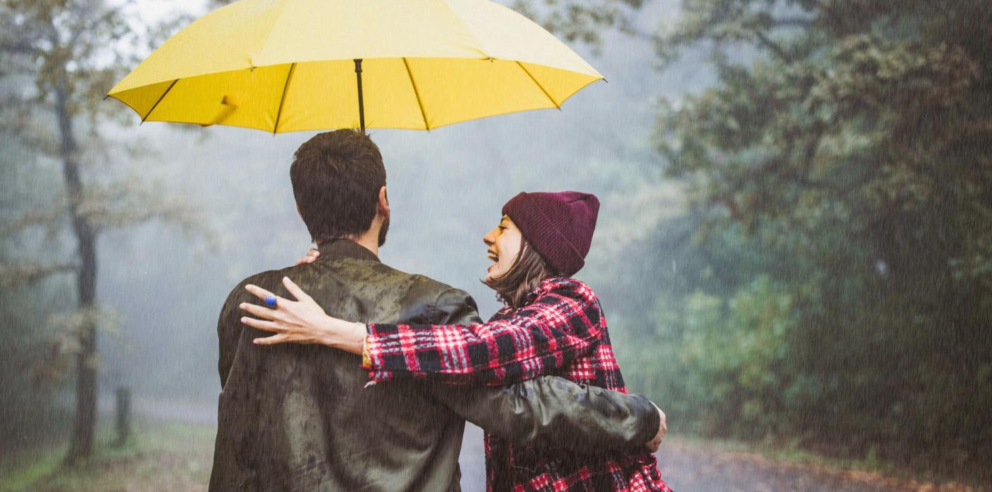 Una coppia felice si abbraccia di spalle riparandosi dalla pioggia sotto un ombrello giallo, che richiama quello iconico di How I Met Your Mother, legato alla Lebenslangerschicksalsschatz di Ted Mosby