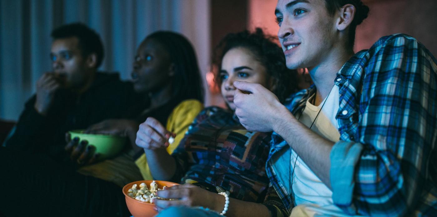 Quattro ragazzi seduti su un divano al buio guardano una serie tv mangiando popcorn