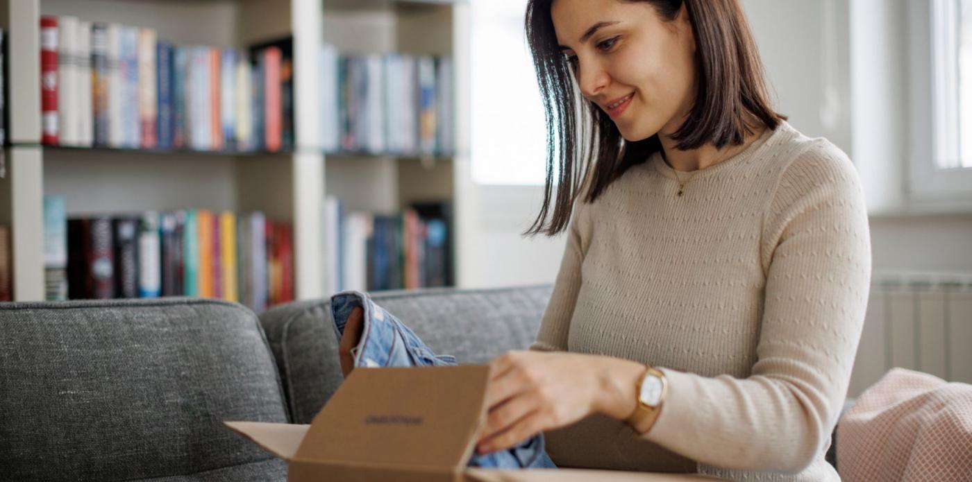 Una donna seduta in soggiorno apre una box letteraria davanti a una libreria