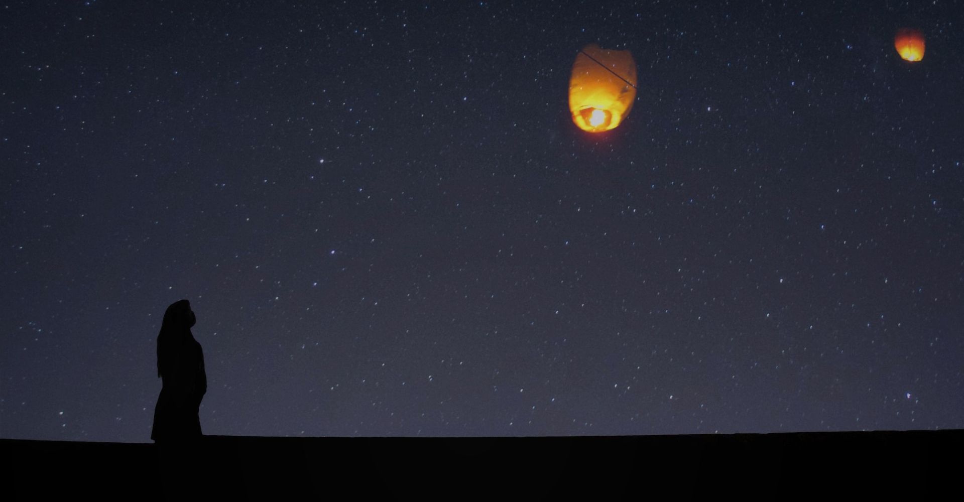 Silhouette di una ragazza di profilo che osserva il cielo stellato e delle lanterne luminose