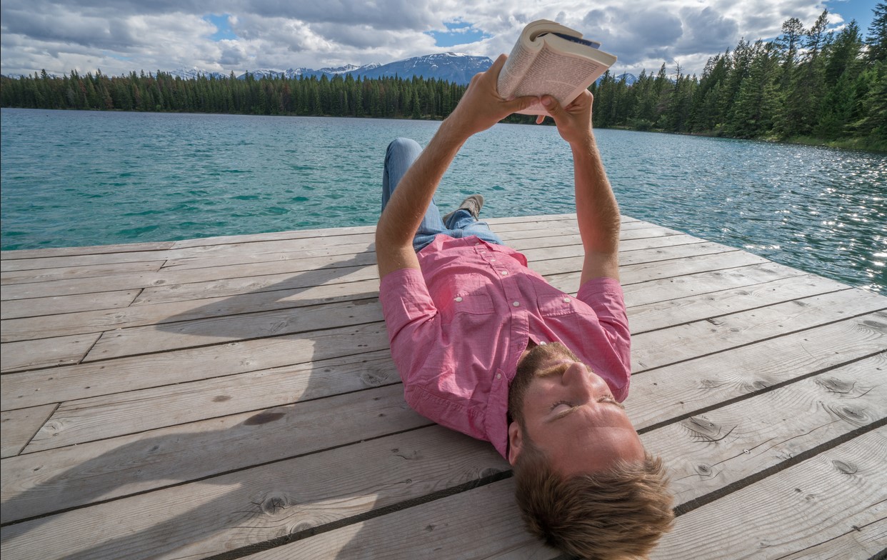 libri da leggere estate 2025, lettore legge libro al lago in montagna