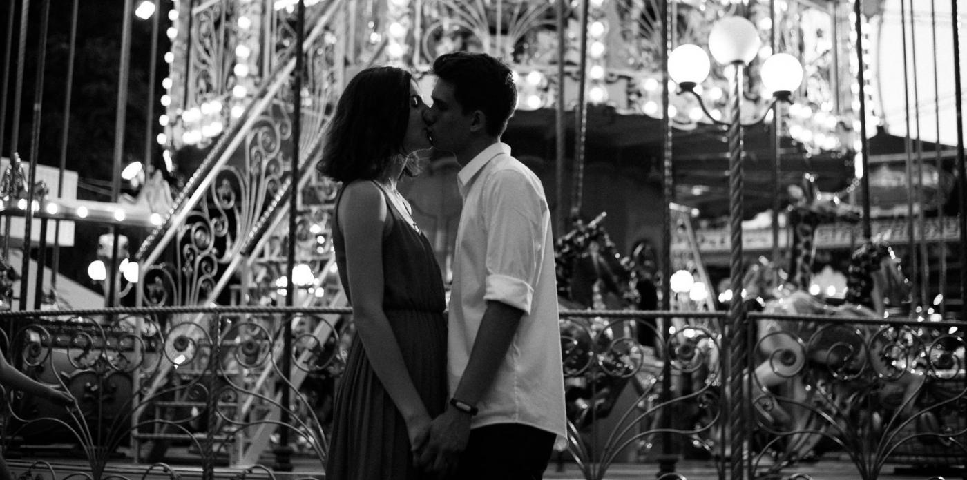 Una foto in bianco e nero di ragazzo e una ragazza che si baciano, di fronte a una giostra, in apertura della selezione di libri sul primo amore