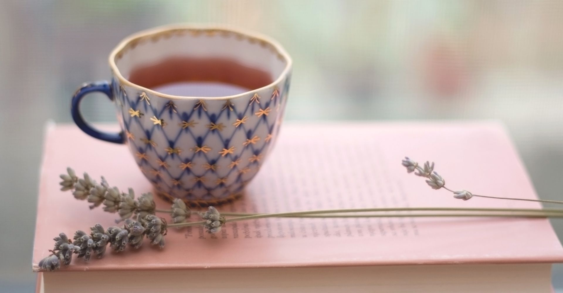 Una tazza di tè poggiata sopra un libro aperto e accanto a un ramoscello di lavanda