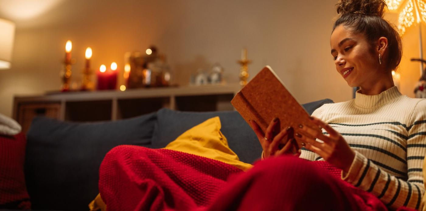 Una ragazza che legge un comfort book sul divano, immersa in un'atmosfera invernale e natalizia