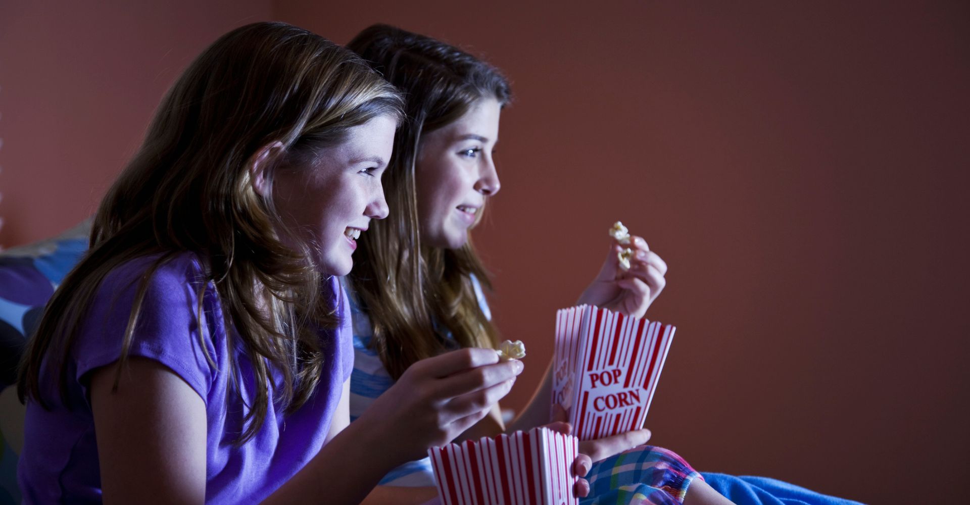 Due ragazze sedute di profilo mangiano dei popcorn mentre lasciano intendere di guardare con attenzione una serie tv