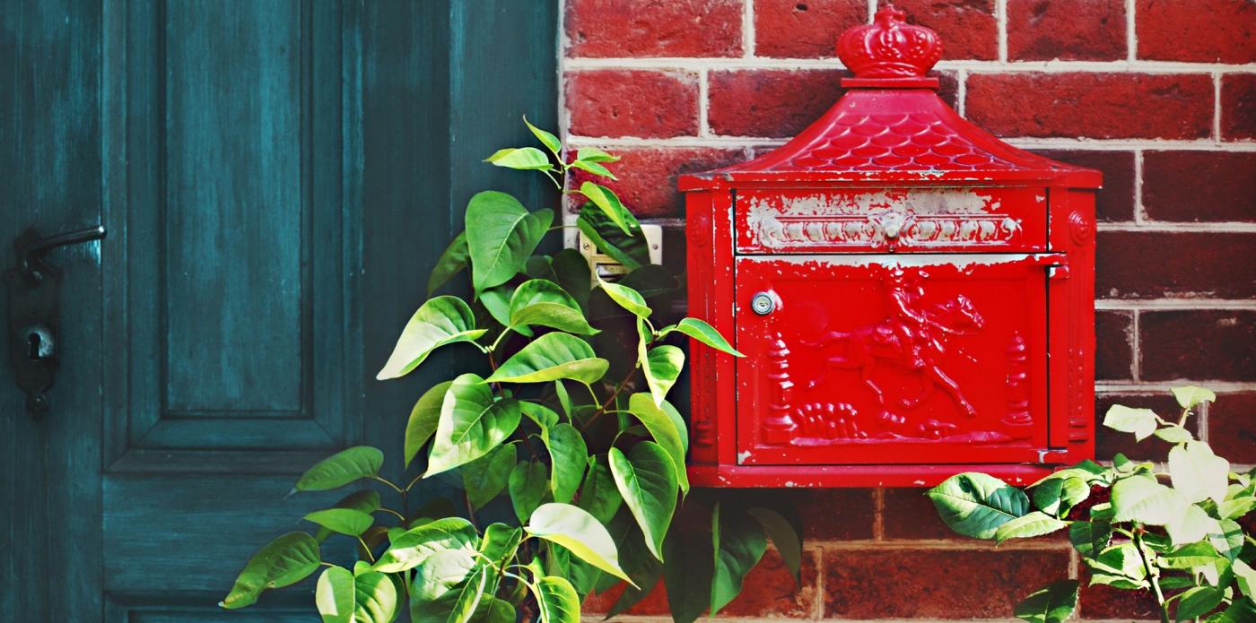 Una cassetta delle lettere rosse su un muro di mattoni, accanto alla porta d'ingresso di una villetta in stile inglese