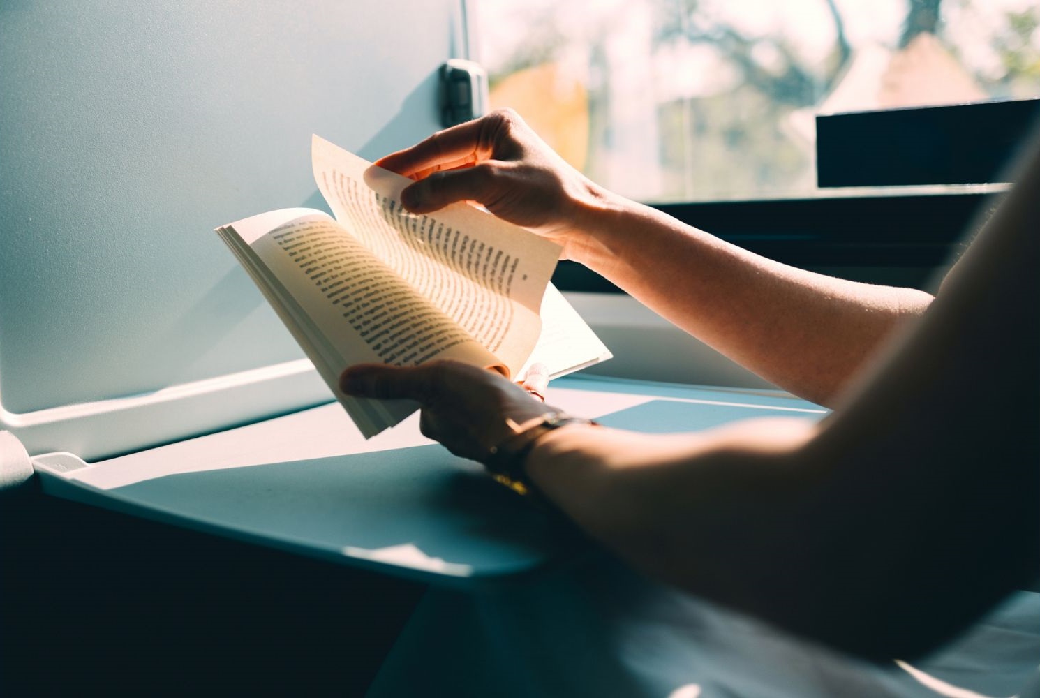 Close-up delle mani di una ragazza che legge un libro seduta in treno