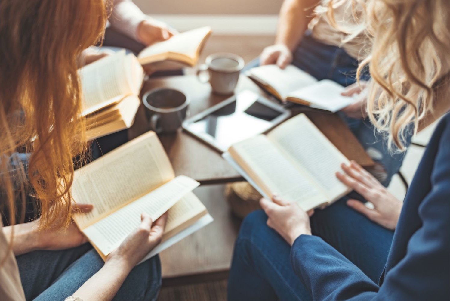 Un gruppo di ragazze e ragazzi seduti l'uno accanto all'altro tengono sulle gambe un libro aperto, su cui probabilmente si stanno confrontando come all'interno di un bookclub