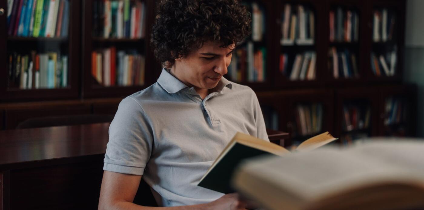 Ragazzo che sorride leggendo un libro in biblioteca