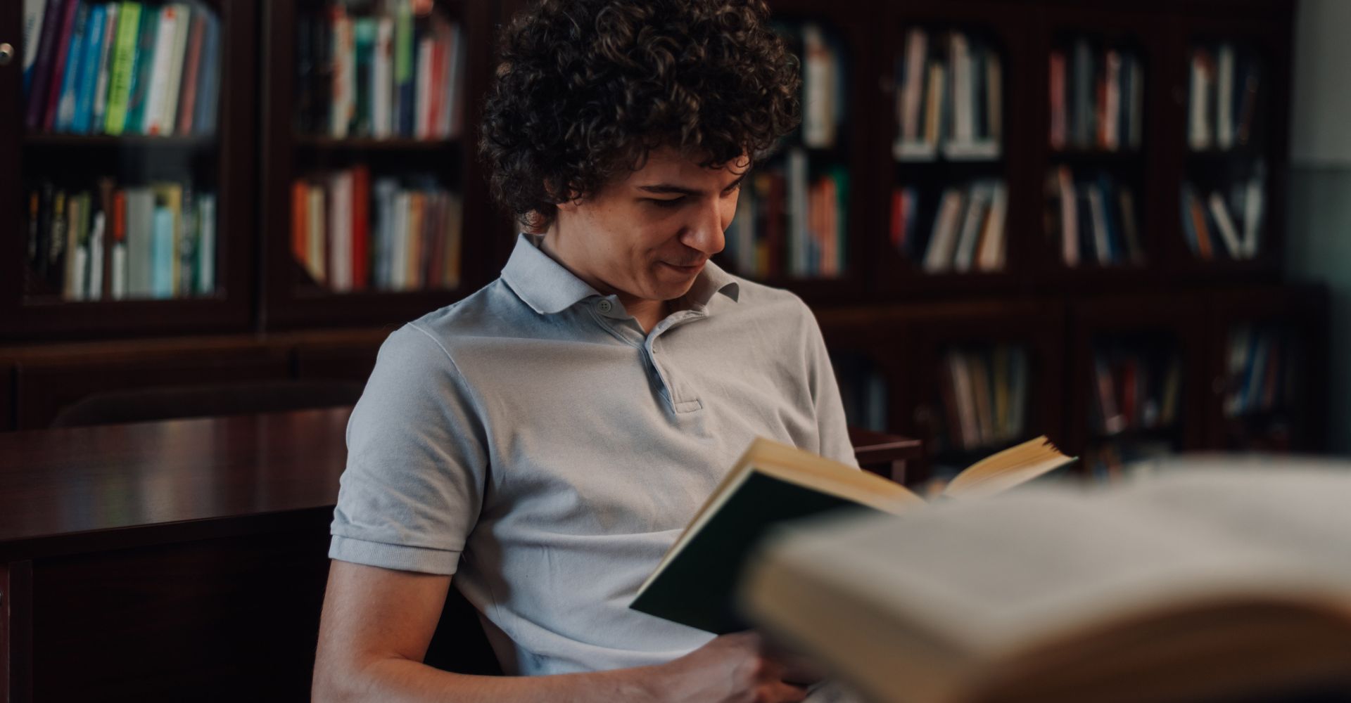 Ragazzo che sorride leggendo un libro in biblioteca
